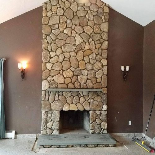 A stone fireplace in a room with a brown wall.